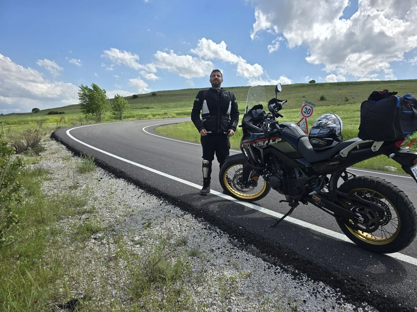 Yeşil tepelerin arasında kıvrılan yolun kenarında, motosikletin yanında