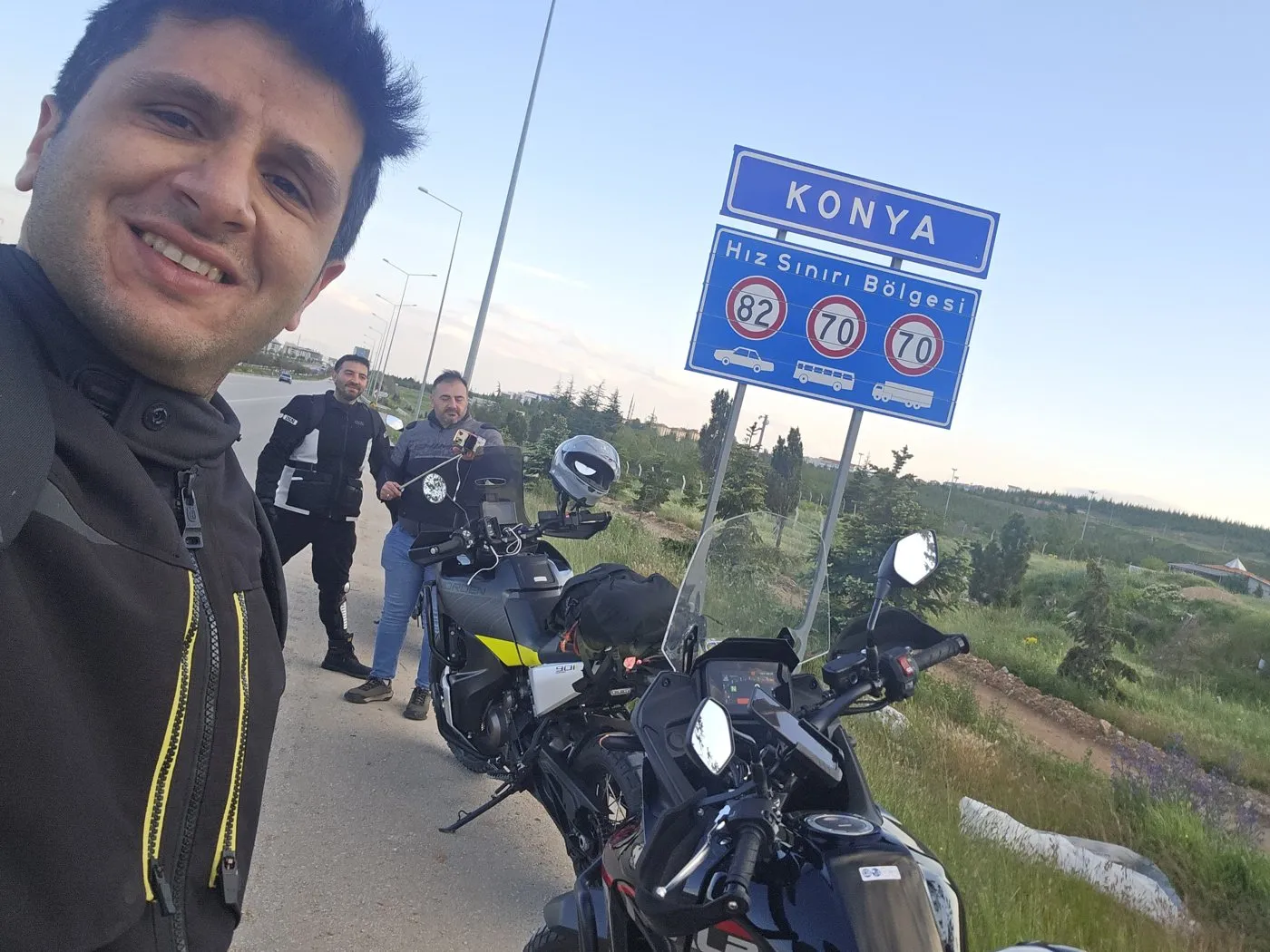 Konya tabelasının önünde üç kişi ve üç motosiklet