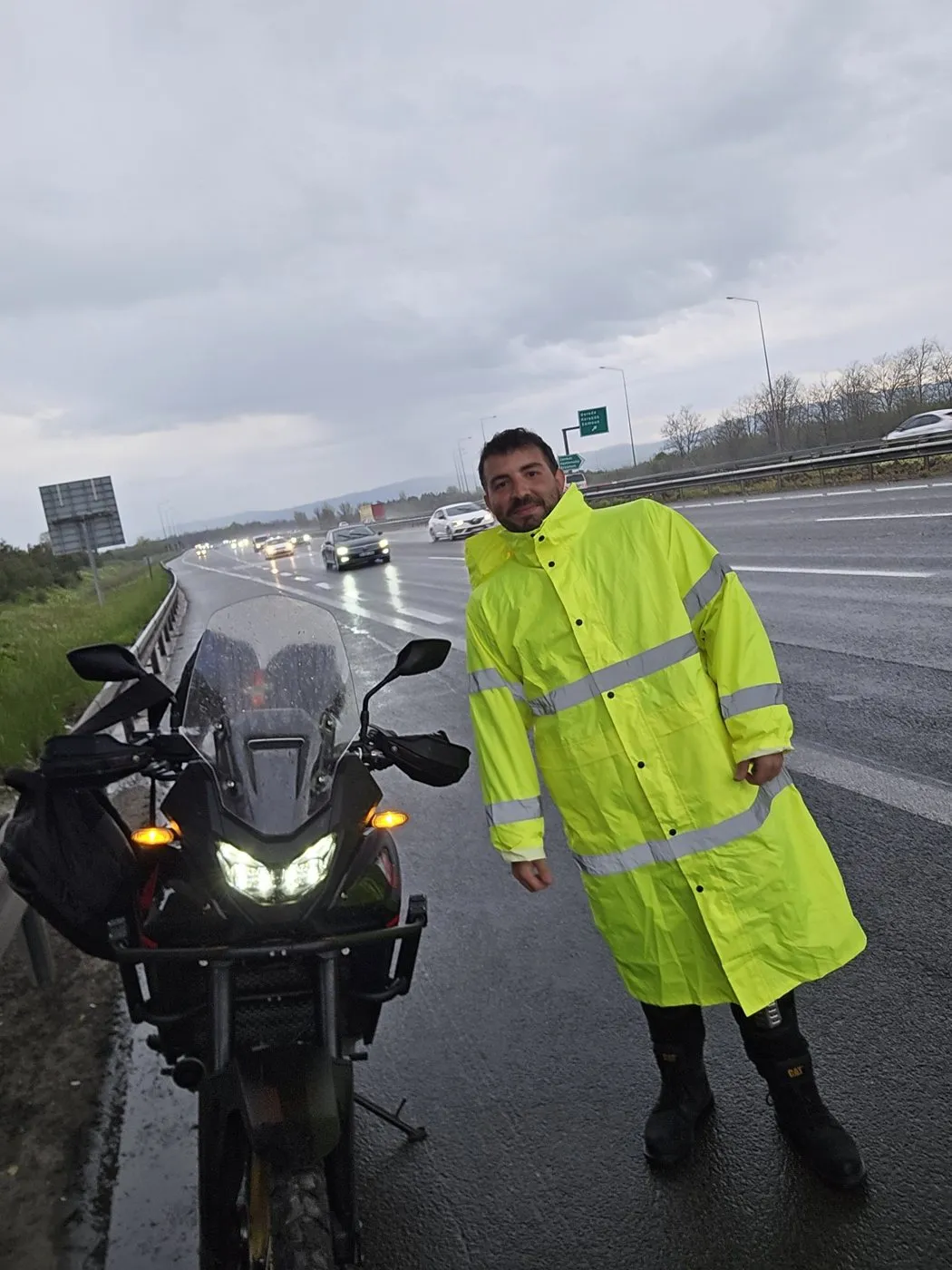 Otoyol kenarında sarı yağmurlukla, farları yanan motosikletin önünde