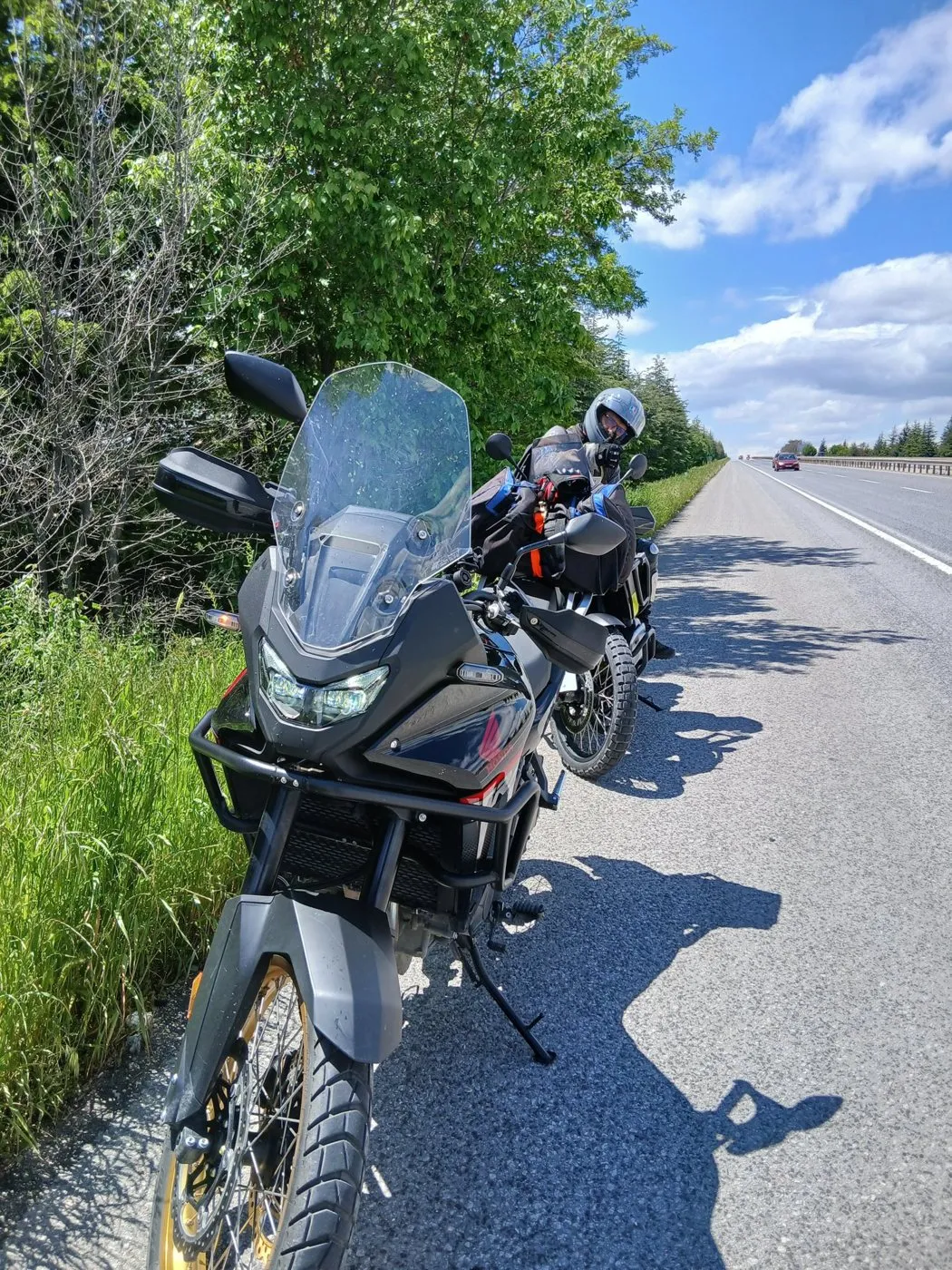 Yol kenarında durdurulmuş motosiklet, arkada ağaçlar ve boş yol